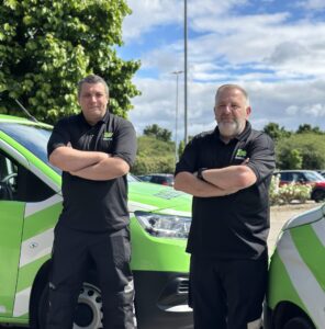 Rob and Noel, standing crossed armed in front of Green Flag vans